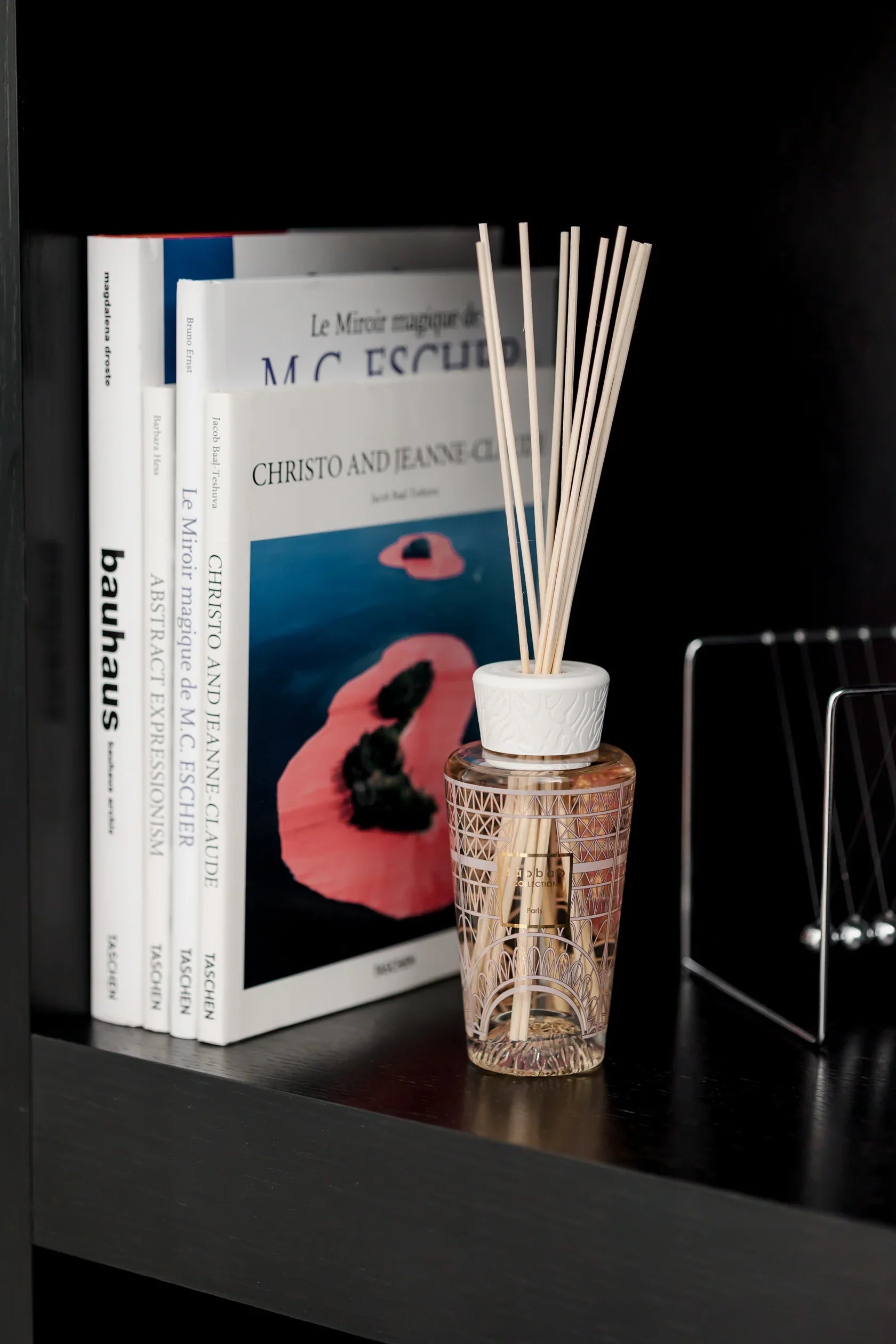 Baobab Collection My First Baobab diffuser on a shelf with books, featuring Eiffel Tower design and reed sticks.