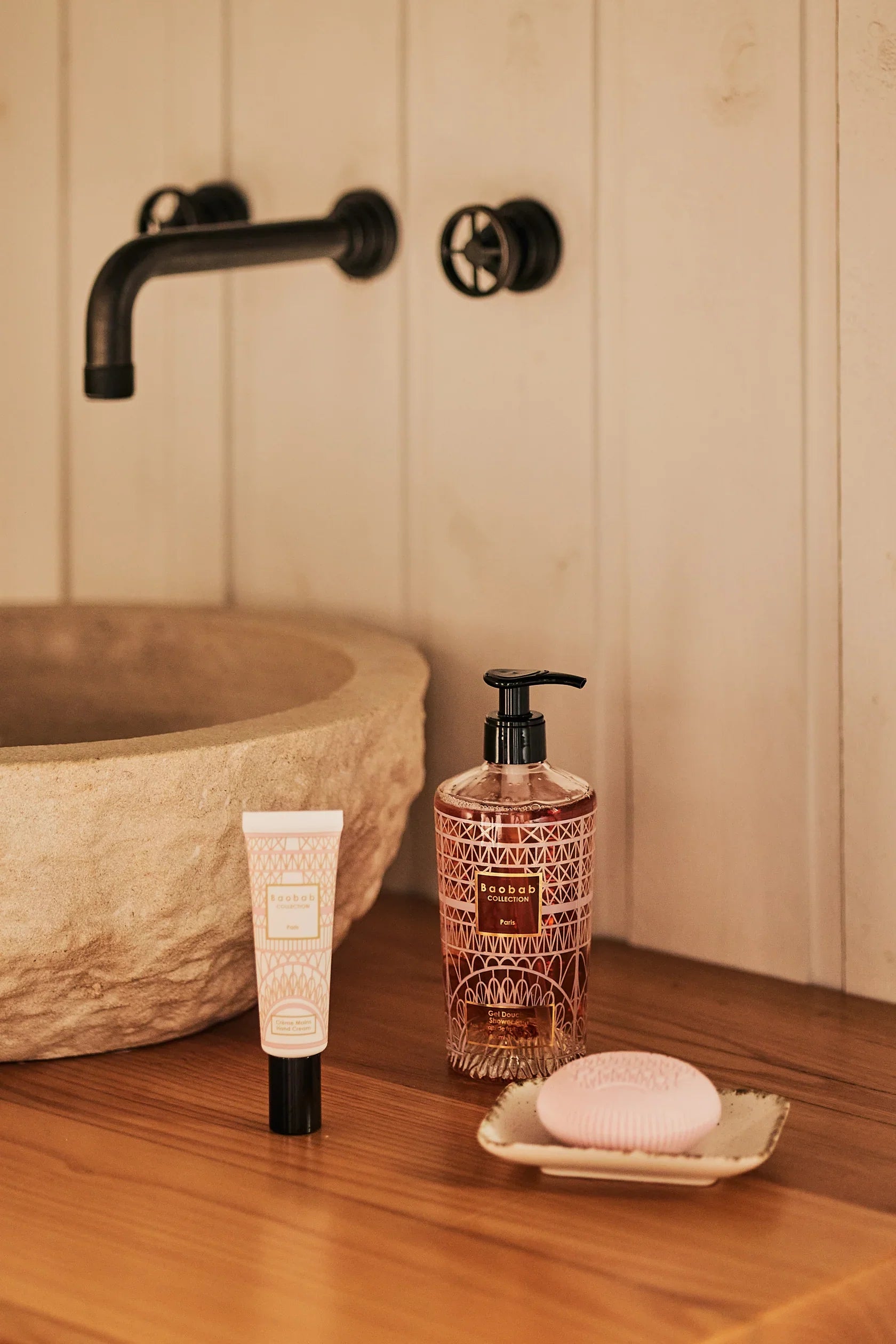 Baobab Collection Paris hand wash and lotion on wooden vanity with stone sink and black faucet.