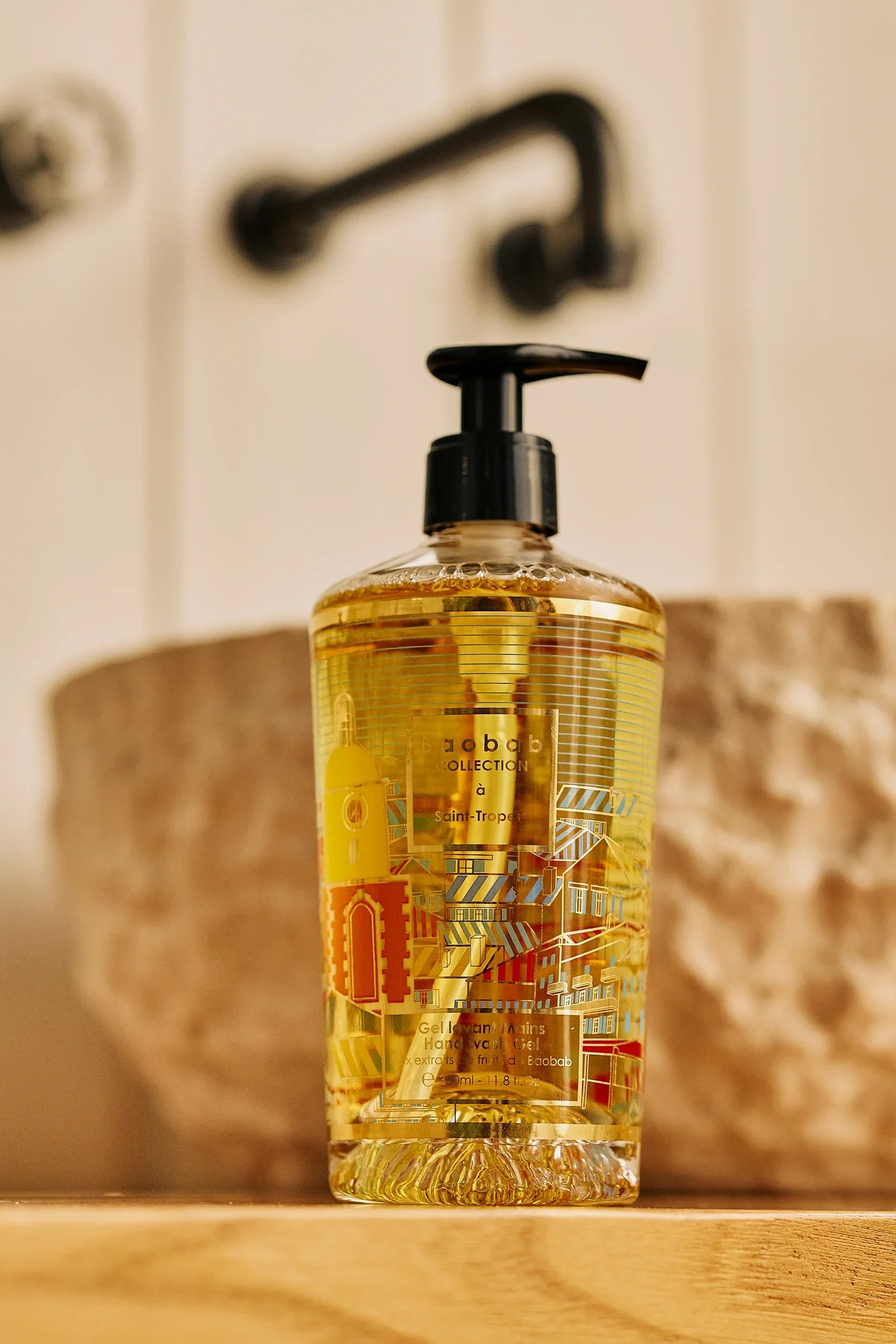 Baobab Collection hand wash gel in stylish bottle, featuring Saint-Tropez design and sunny yellow gel, on wooden surface.