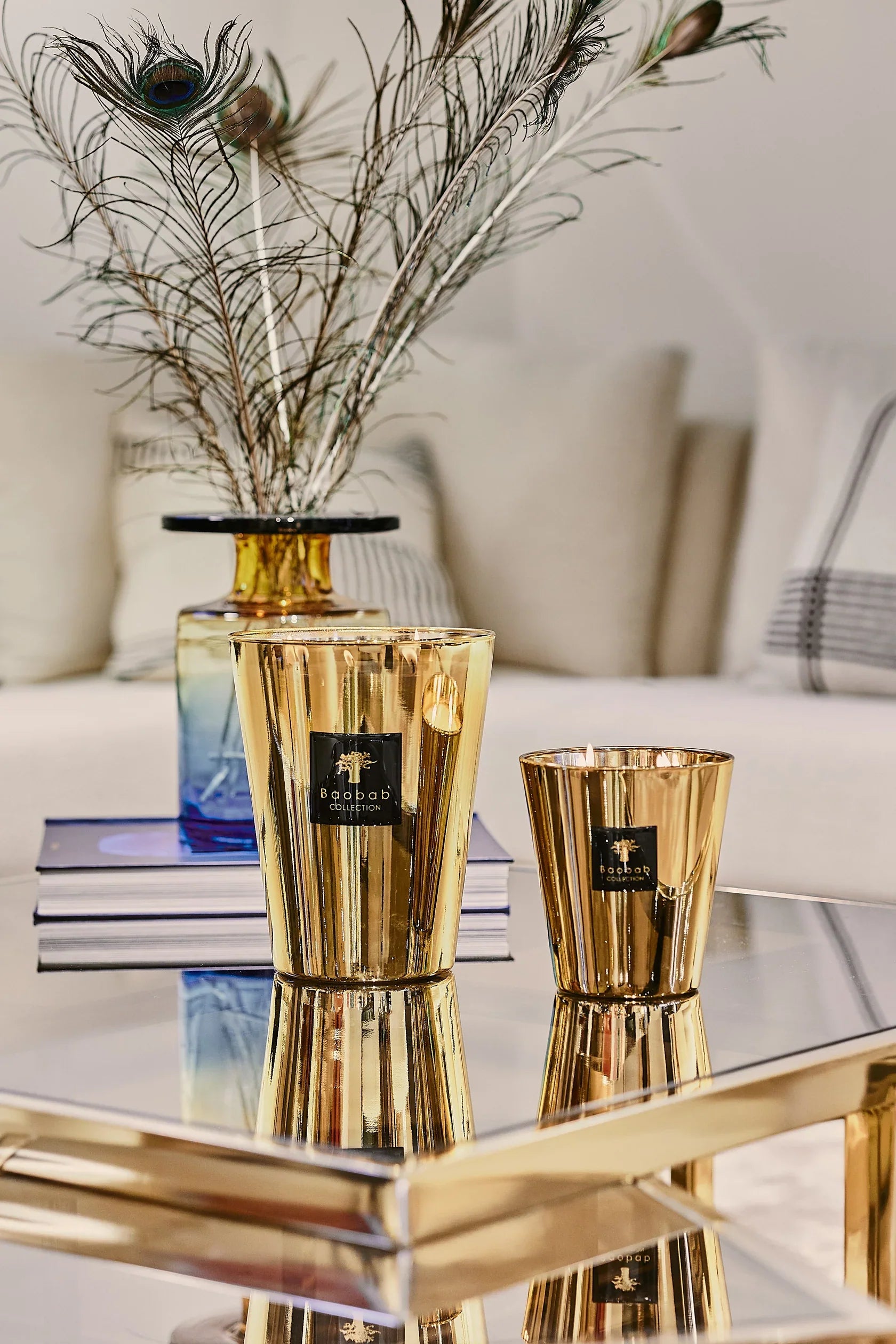 Golden Baobab Collection candles displayed elegantly on a mirrored tray, surrounded by decorative peacock feathers.
