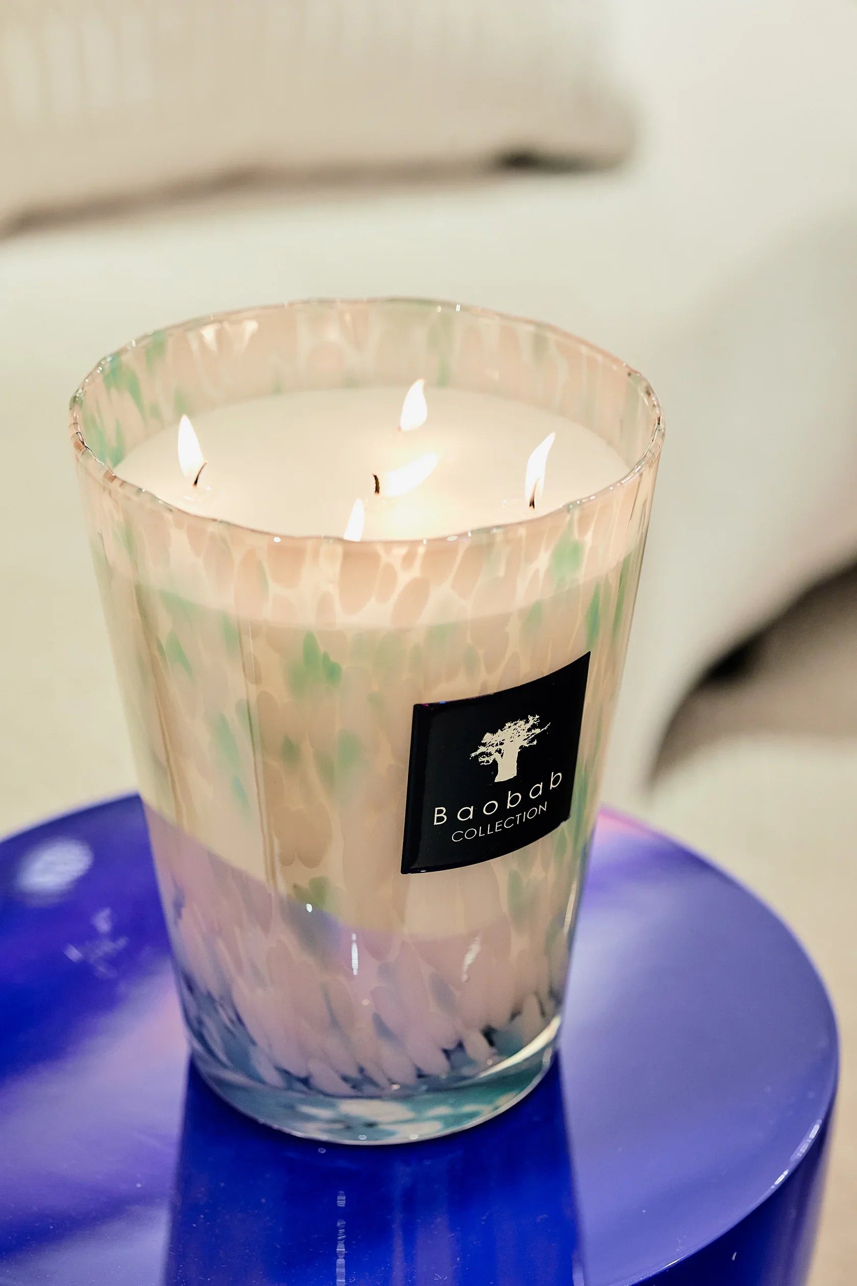 Baobab Collection Sapphire Pearls candle in hand-blown glass with marine scent and colorful details on a blue table.