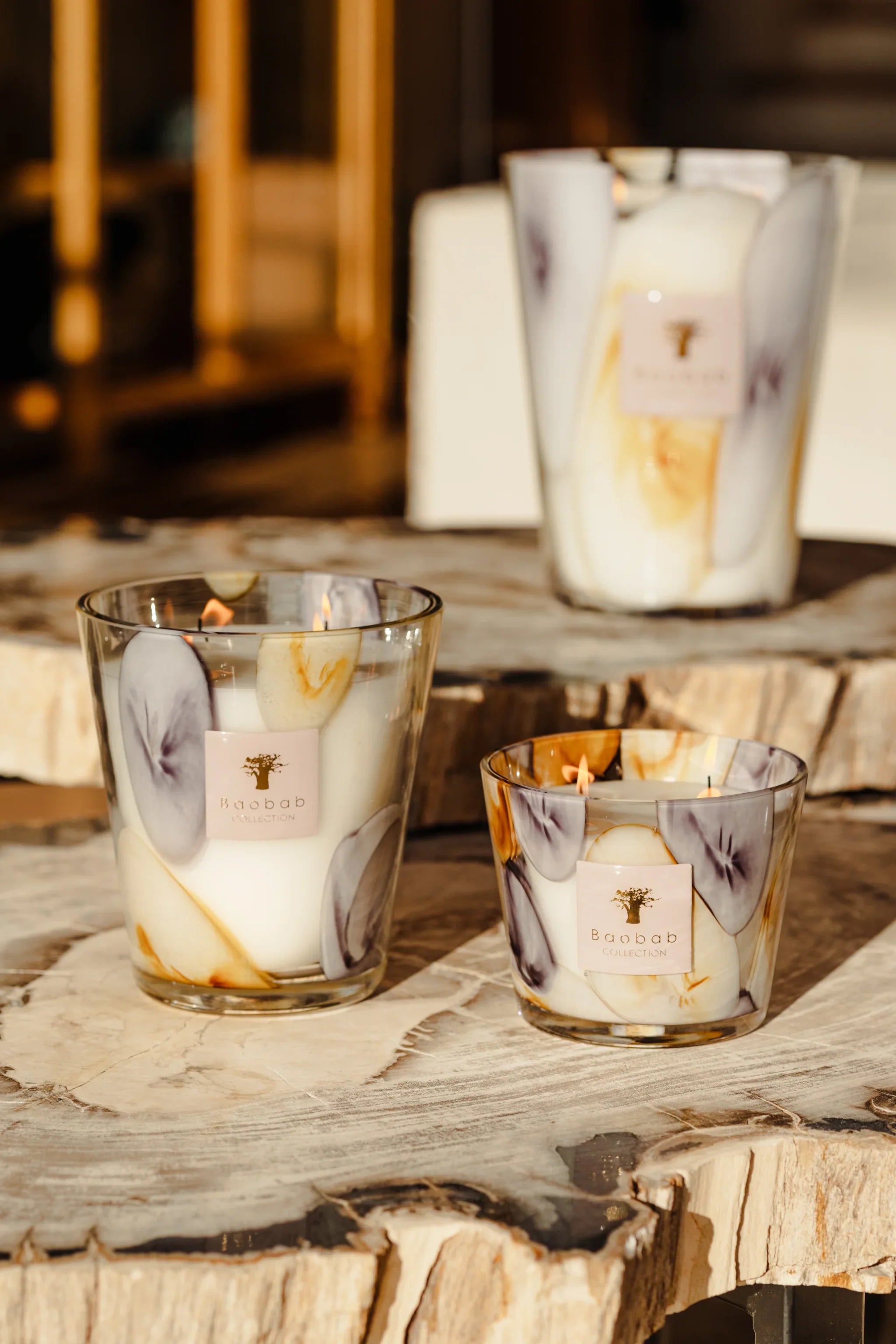 Set of three Baobab Collection scented candles with elegant mauve and saffron designs on wooden surface.