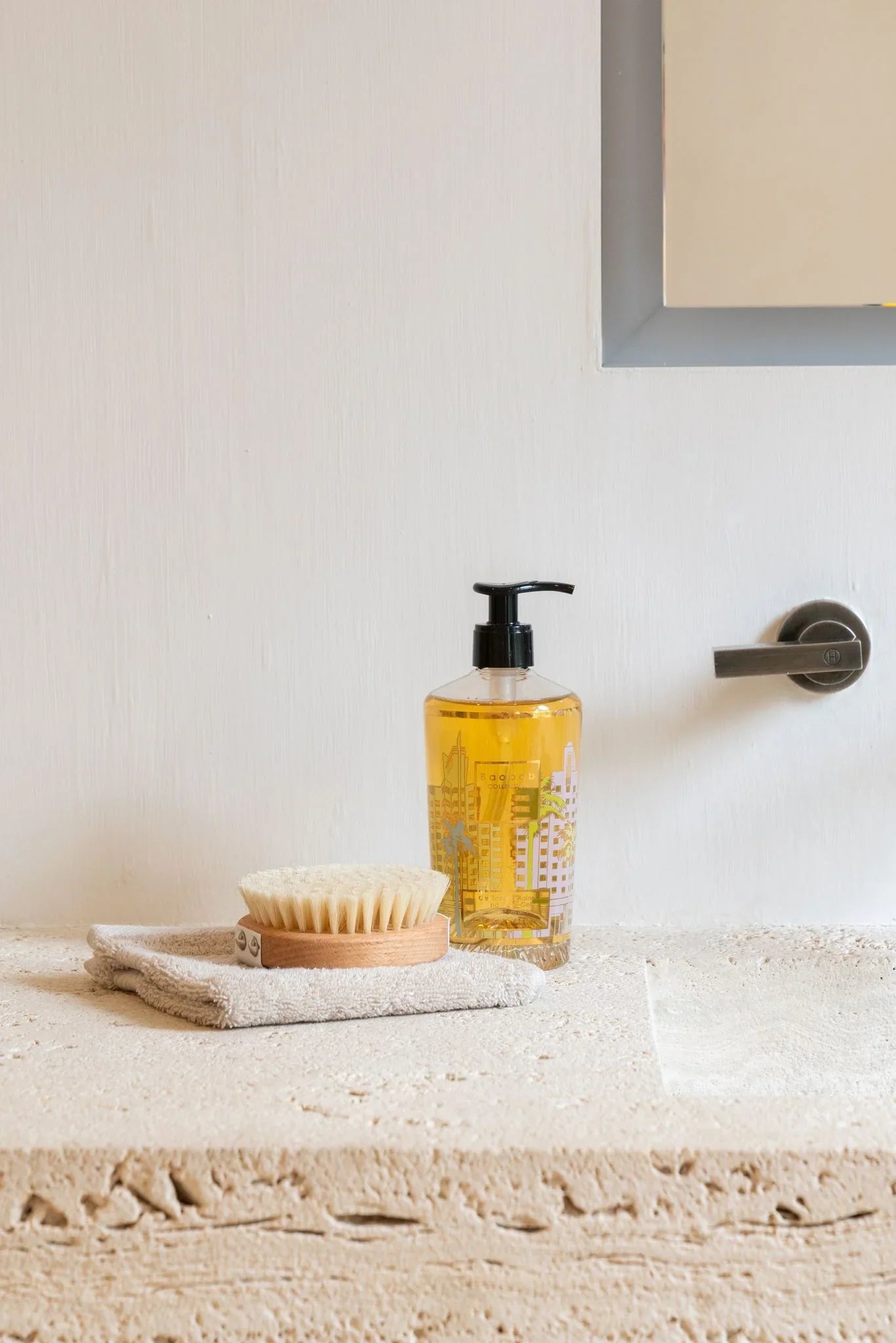 Baobab Collection Miami hand wash gel in a glass bottle on a stone countertop with a bamboo scrub and towel.