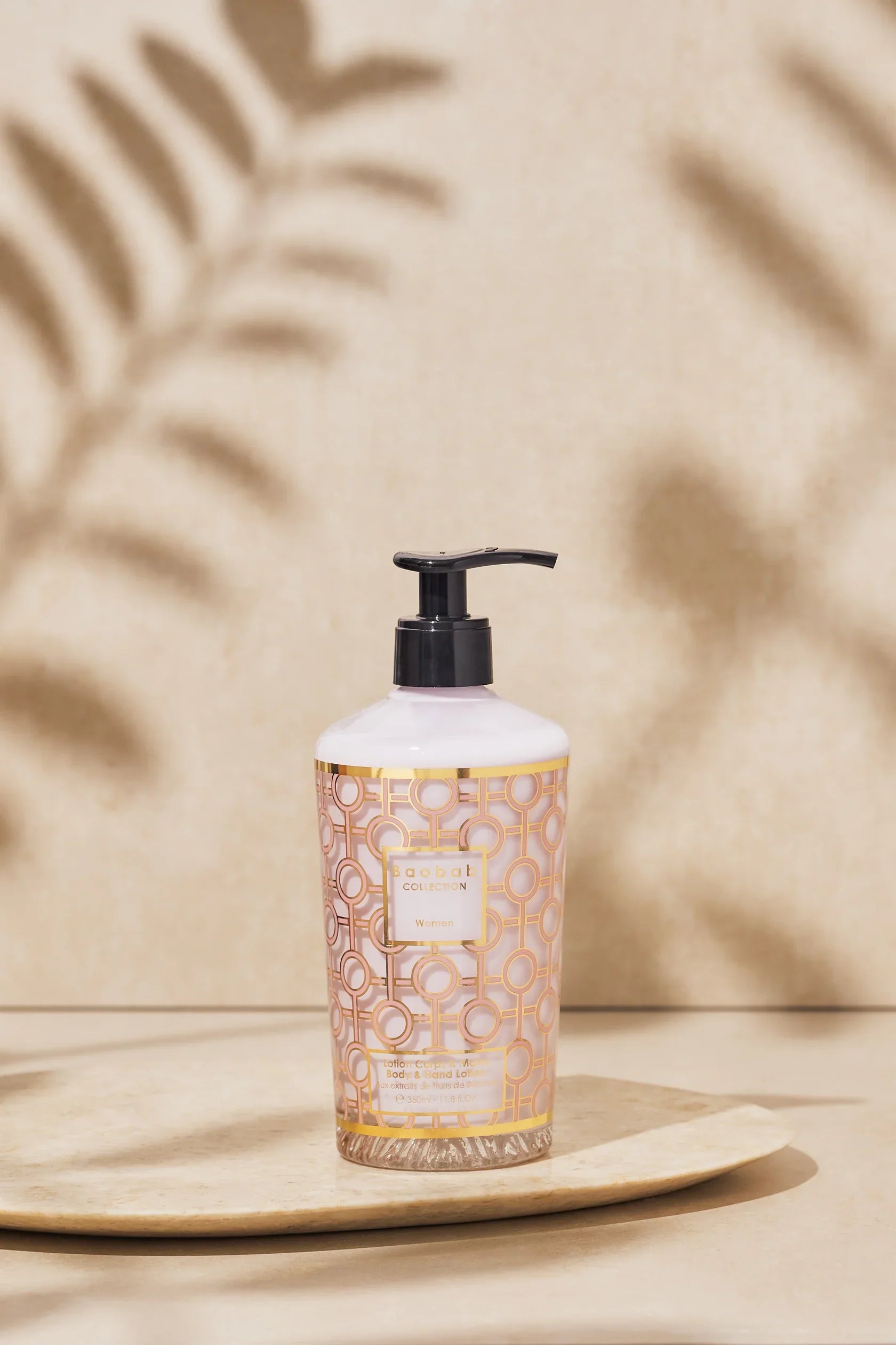 Baobab Collection hand and body lotion bottle on a decorative plate, featuring elegant gold and pink design.