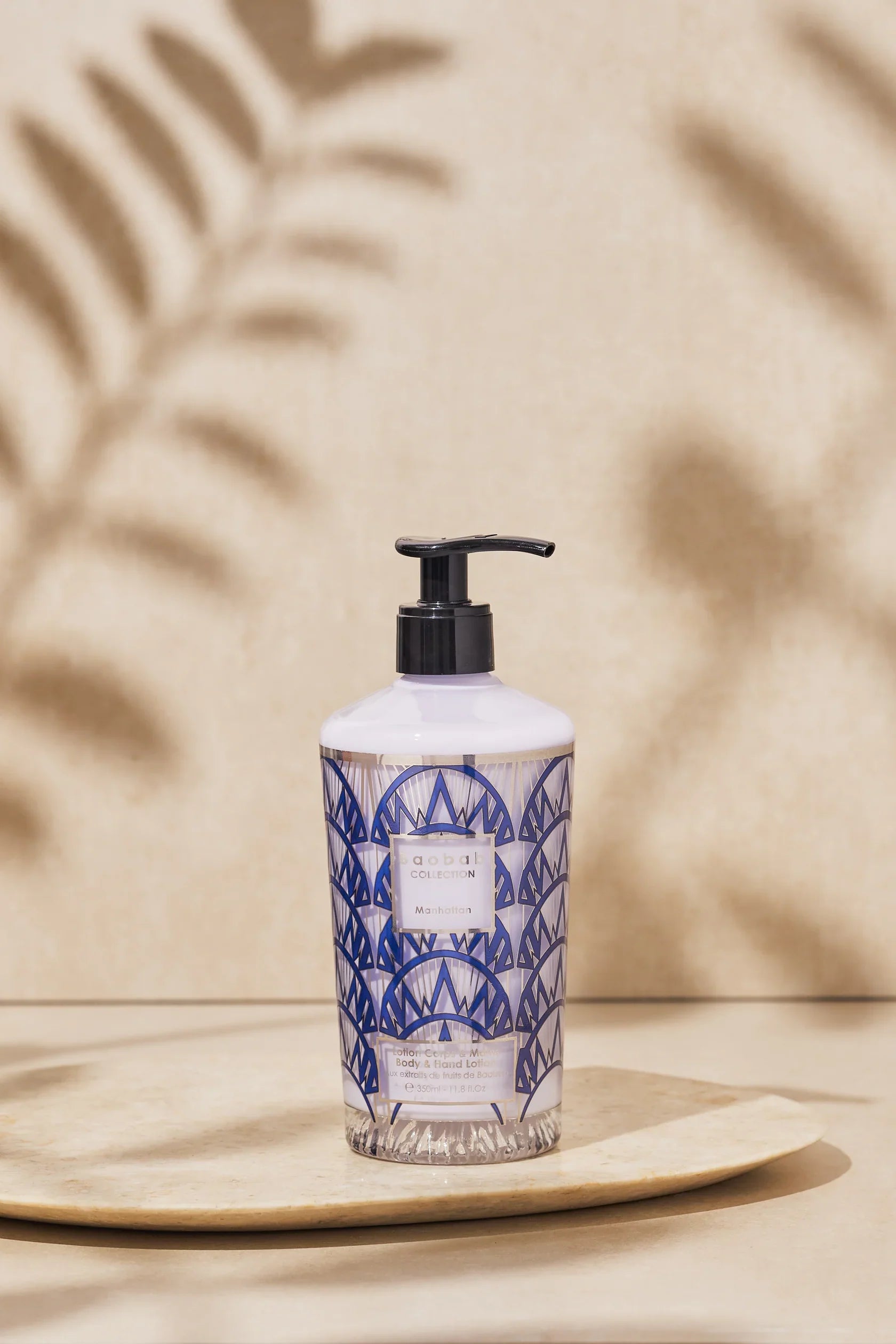 Baobab Collection Manhattan hand and body lotion in decorative bottle on a plate, featuring cream and navy design.