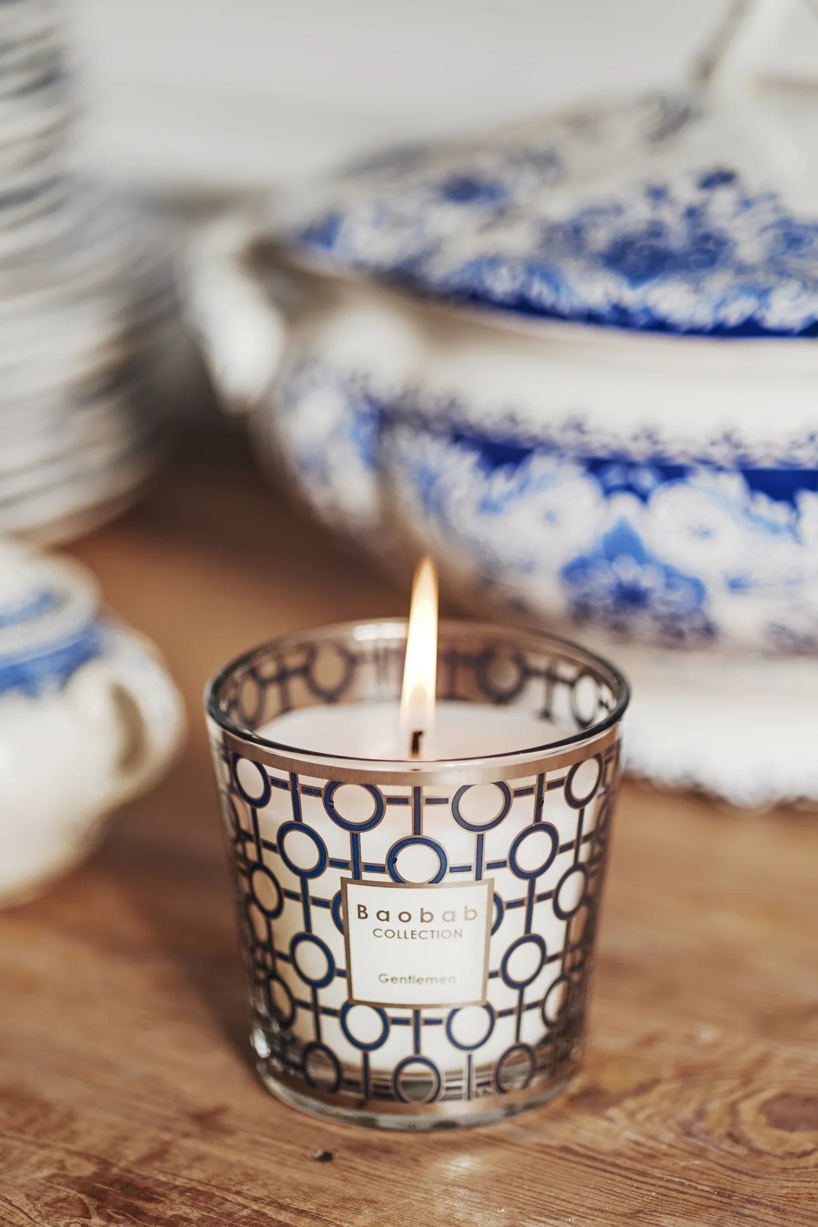 Baobab Collection scented candle 'My First Baobab Gentlemen' with flame, stylish glass design, surrounded by decorative dishes.