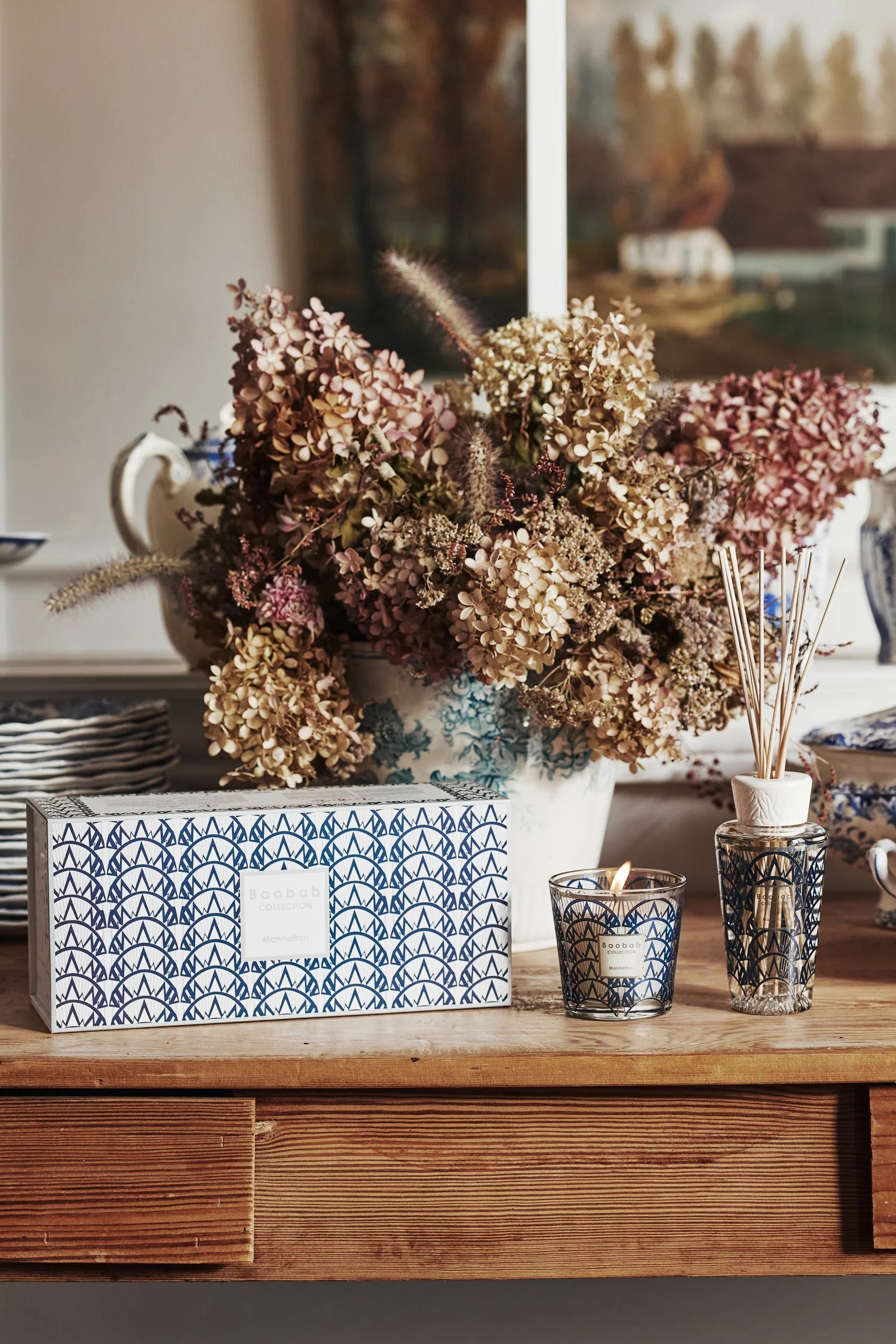 Baobab Collection gift box with Manhattan scented candle and diffuser, decorative floral arrangement in background.
