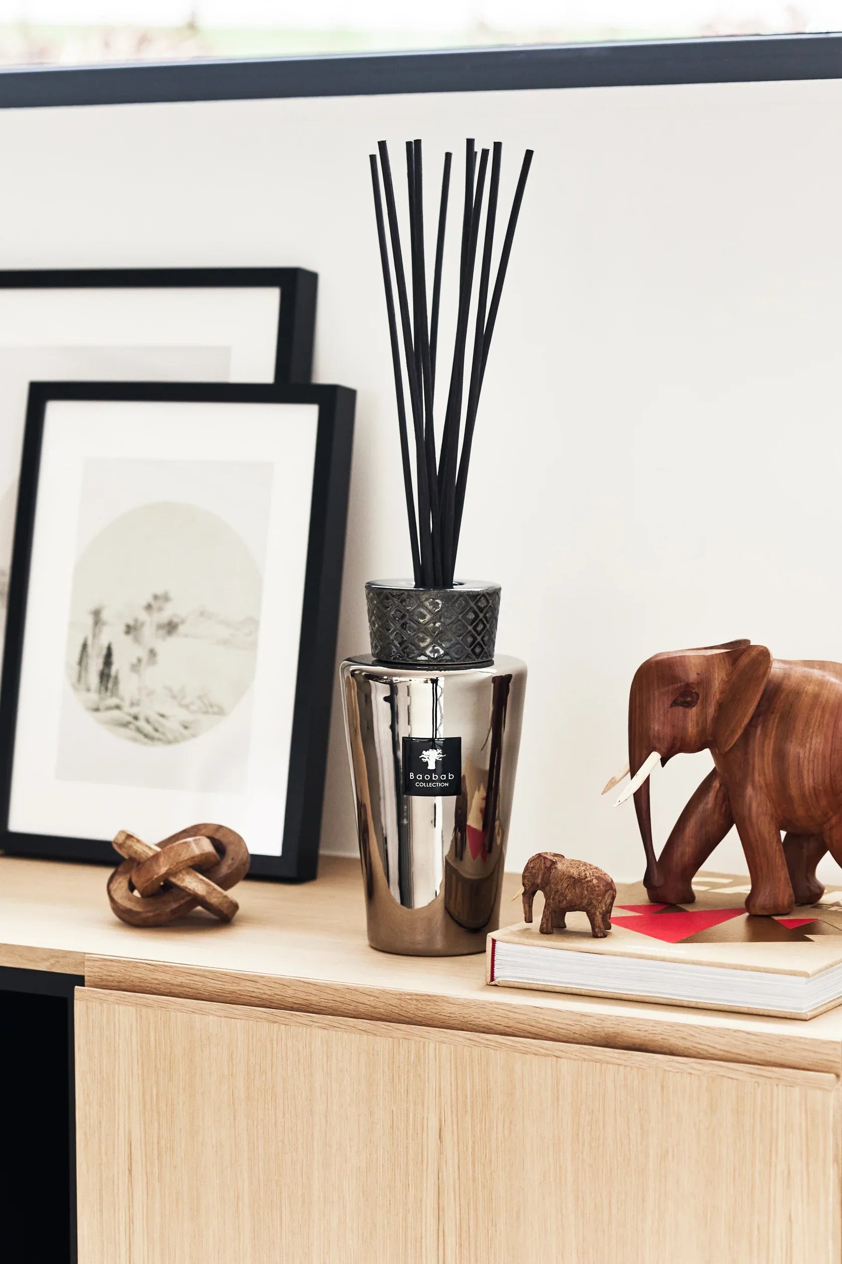 Baobab Collection Totem Platinum diffuser with black sticks on wooden surface, surrounded by decor and art.