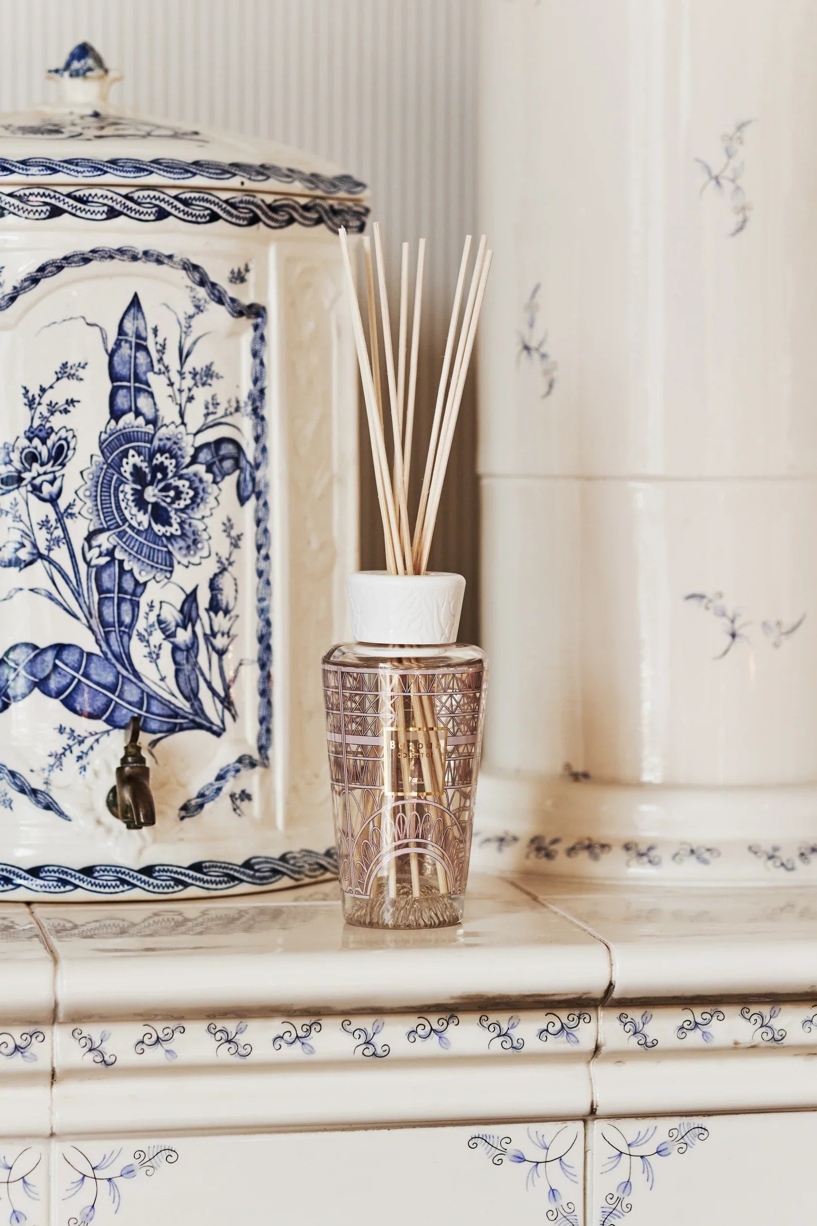 Elegant home fragrance diffuser with reeds on tiled surface next to decorative vase.