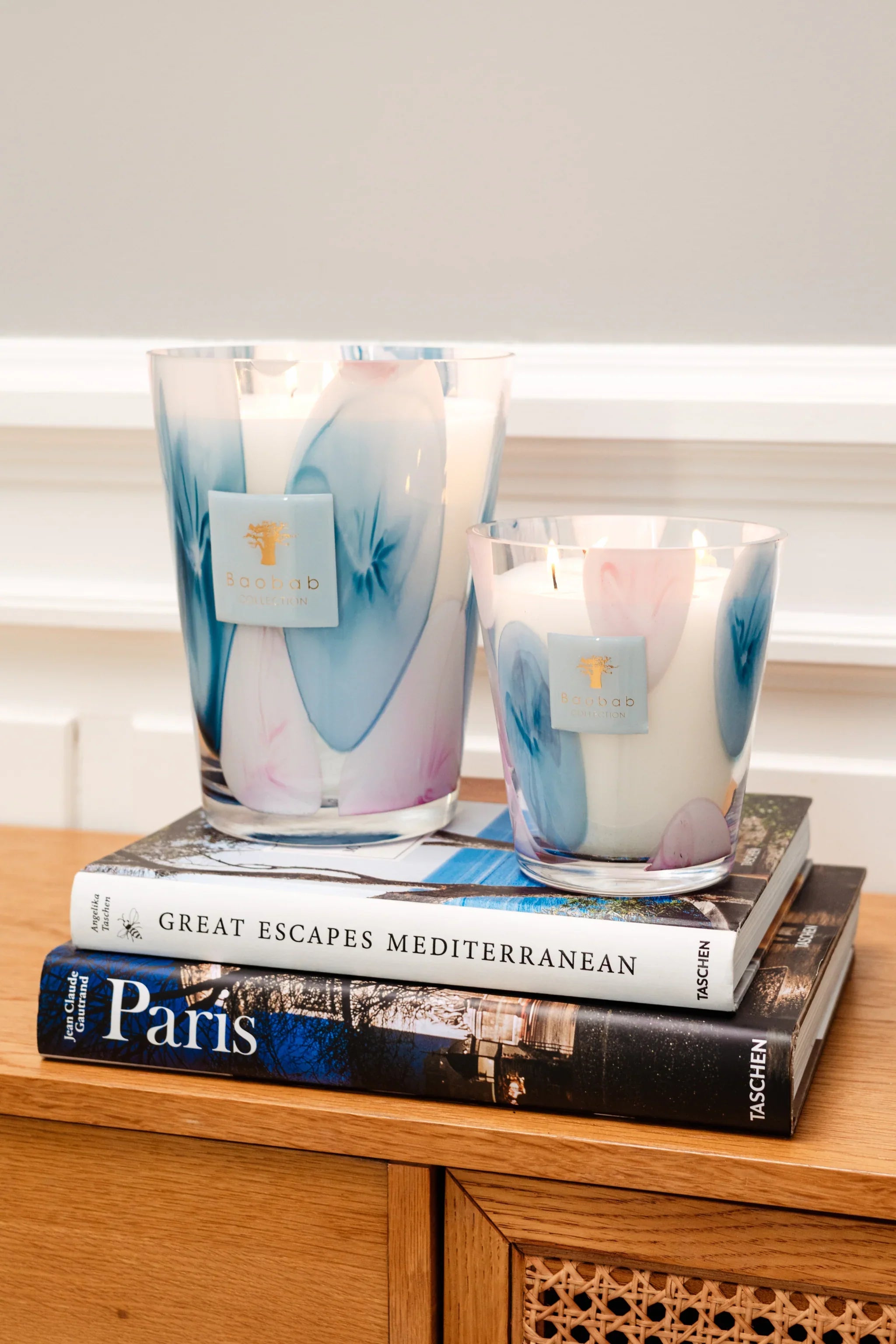 Baobab Collection scented candles in colorful glass on stacked books, adding a stylish touch to any decor.