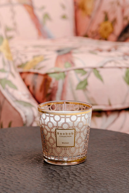 Elegant Baobab Collection women’s candle in a gold and powder pink glass holder on a dark table.