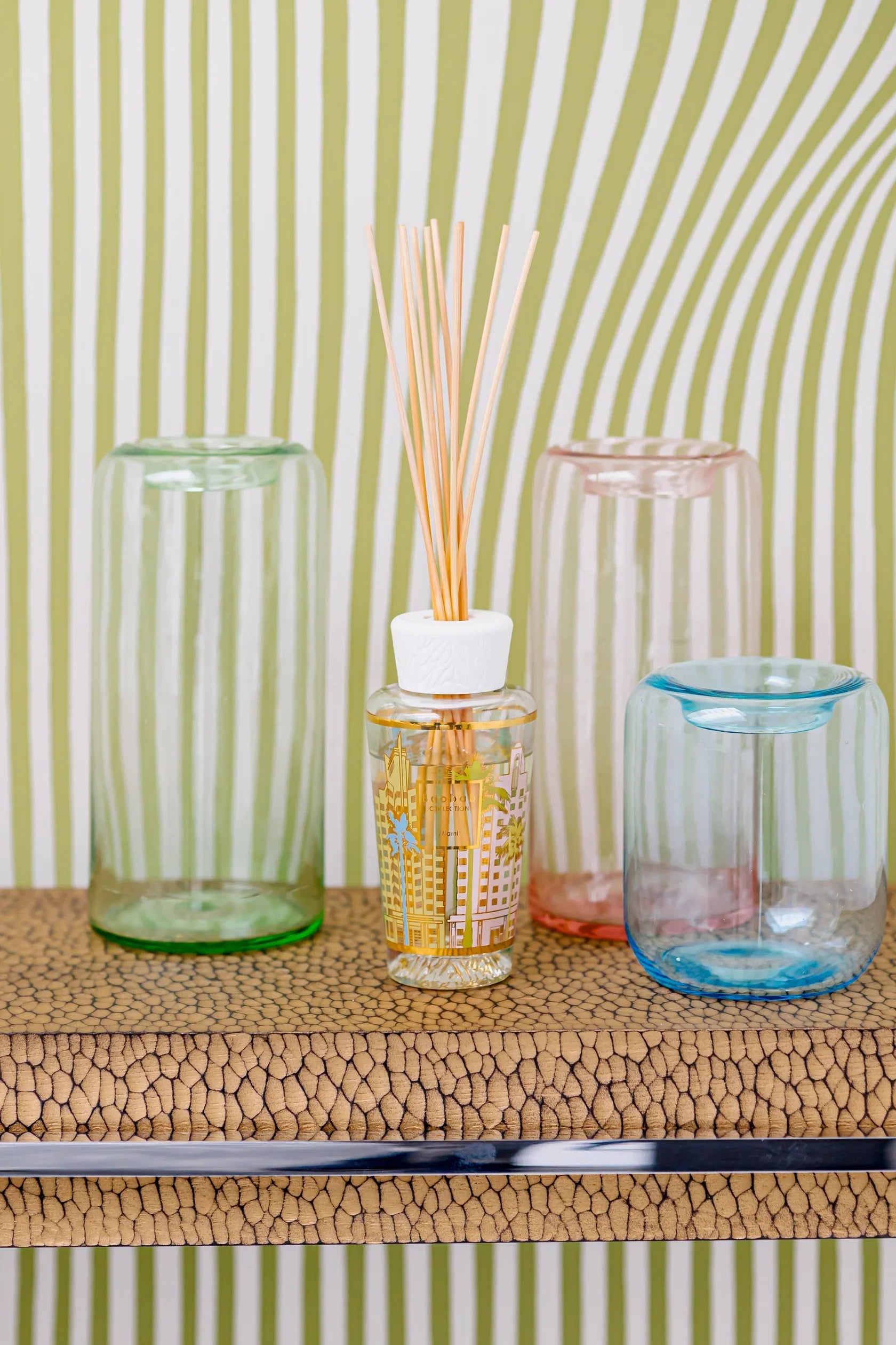 Colorful glass containers with a home fragrance diffuser on a textured surface against a striped background.