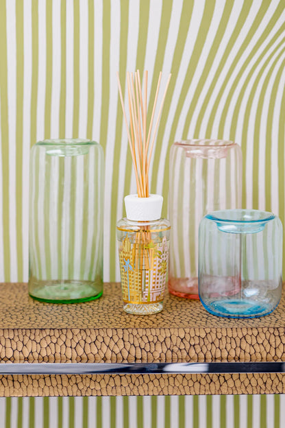 Colorful glass containers with a home fragrance diffuser on a textured surface against a striped background.