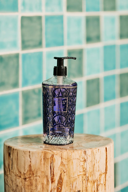 Baobab Collection Manhattan hand wash gel in decorative glass bottle on wooden stool, with turquoise tiled background.