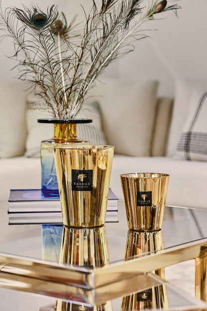 Golden Baobab Collection candles displayed elegantly on a mirrored tray, surrounded by decorative peacock feathers.