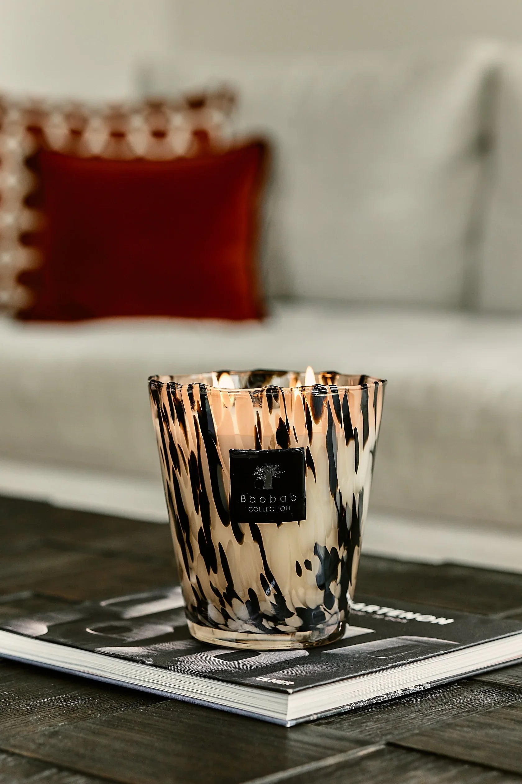 Baobab Collection candle on a coffee table, featuring elegant design and warm glow, surrounded by soft furnishings.