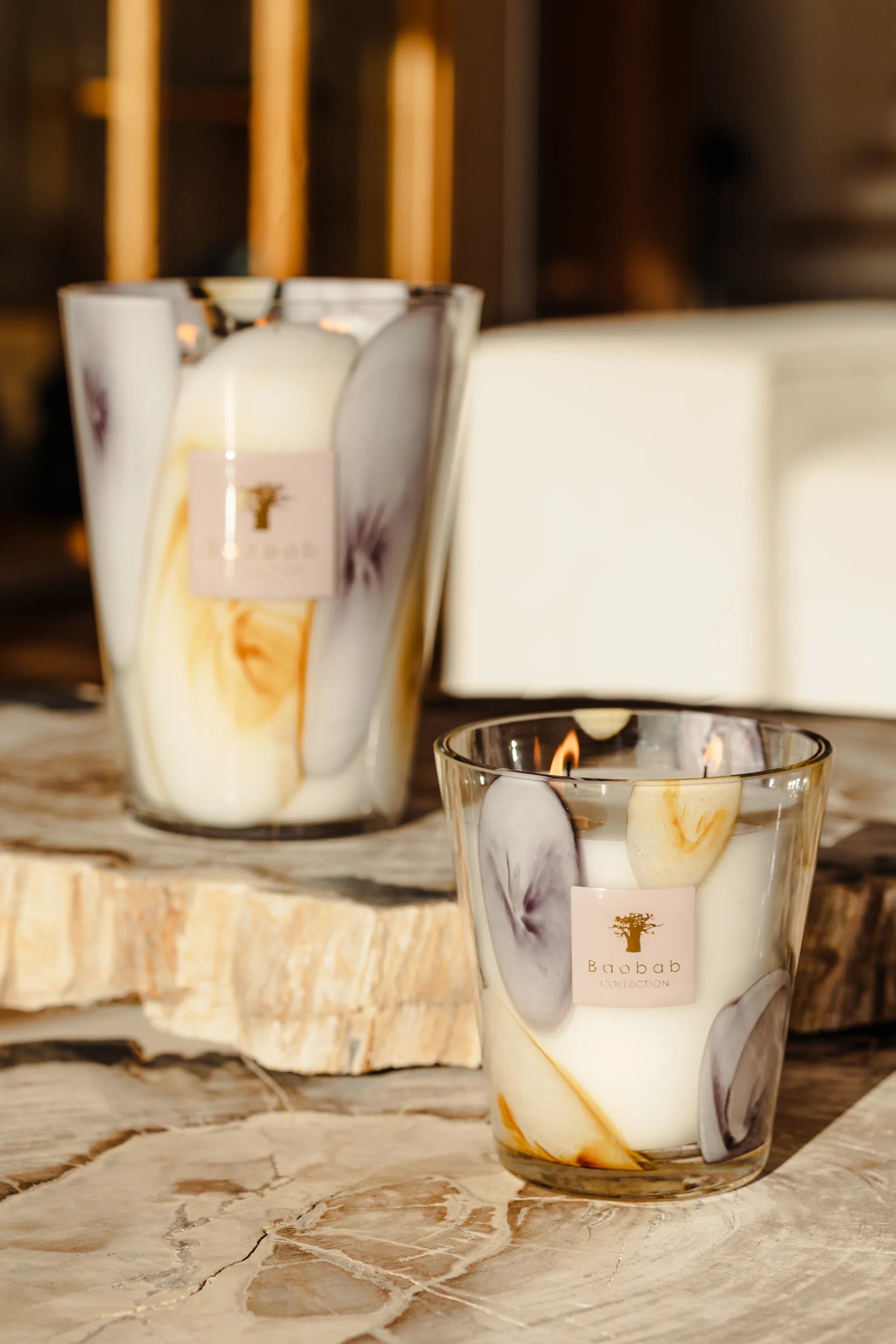 Baobab Collection Eilenroc scented candles in mauve and saffron yellow glass on a stone table.