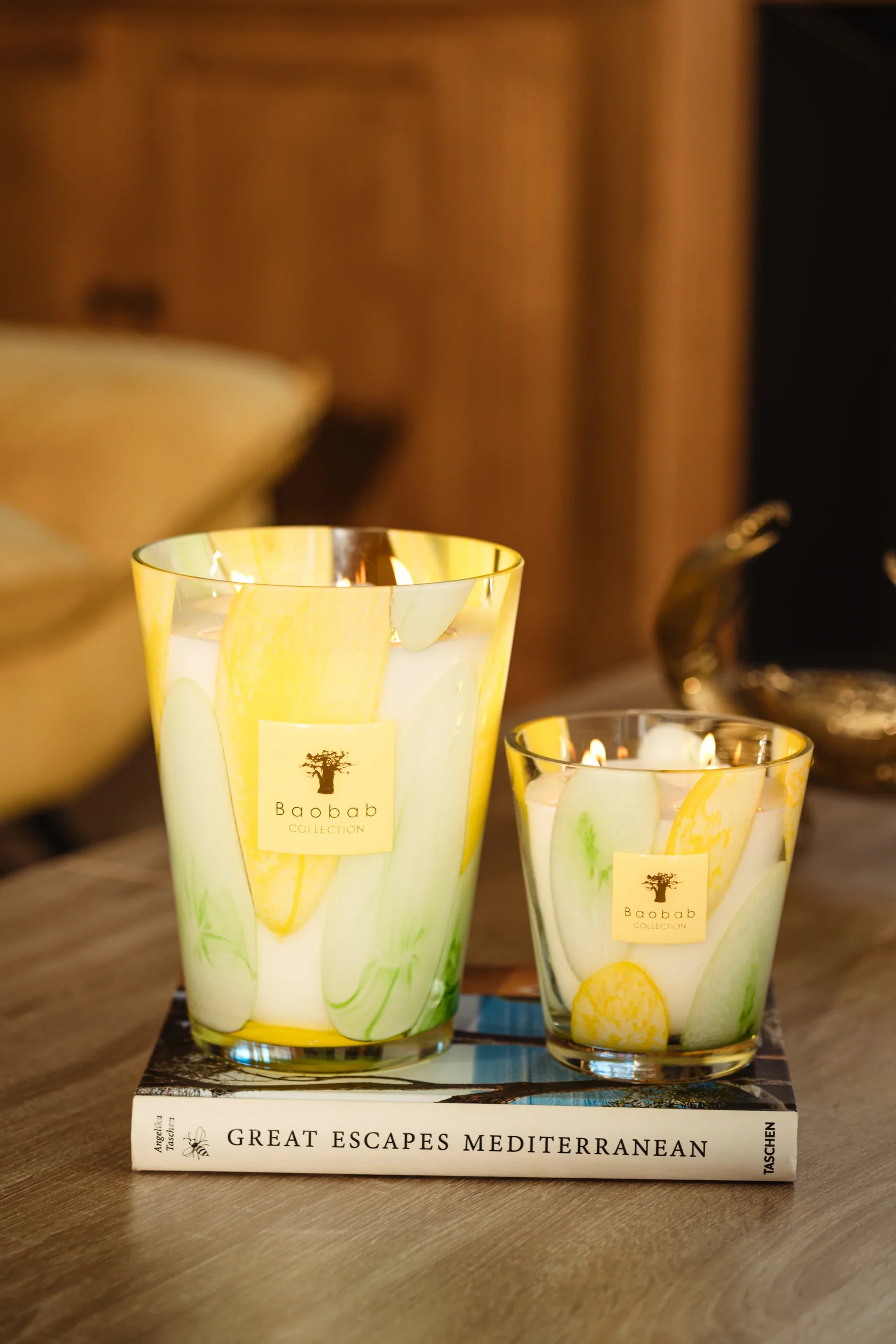 Baobab Collection scented candles in hand-blown glass with yellow and green designs on a coffee table.