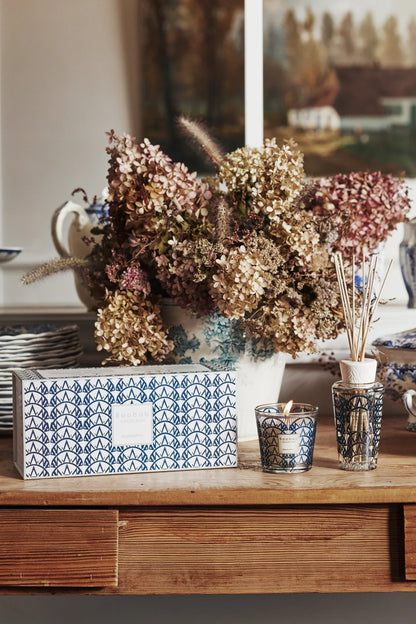 Baobab Collection gift box with Manhattan scented candle and diffuser, decorative floral arrangement in background.