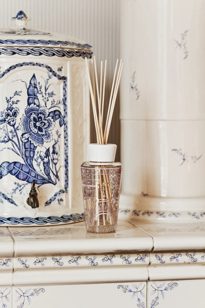 Elegant home fragrance diffuser with reeds on tiled surface next to decorative vase.