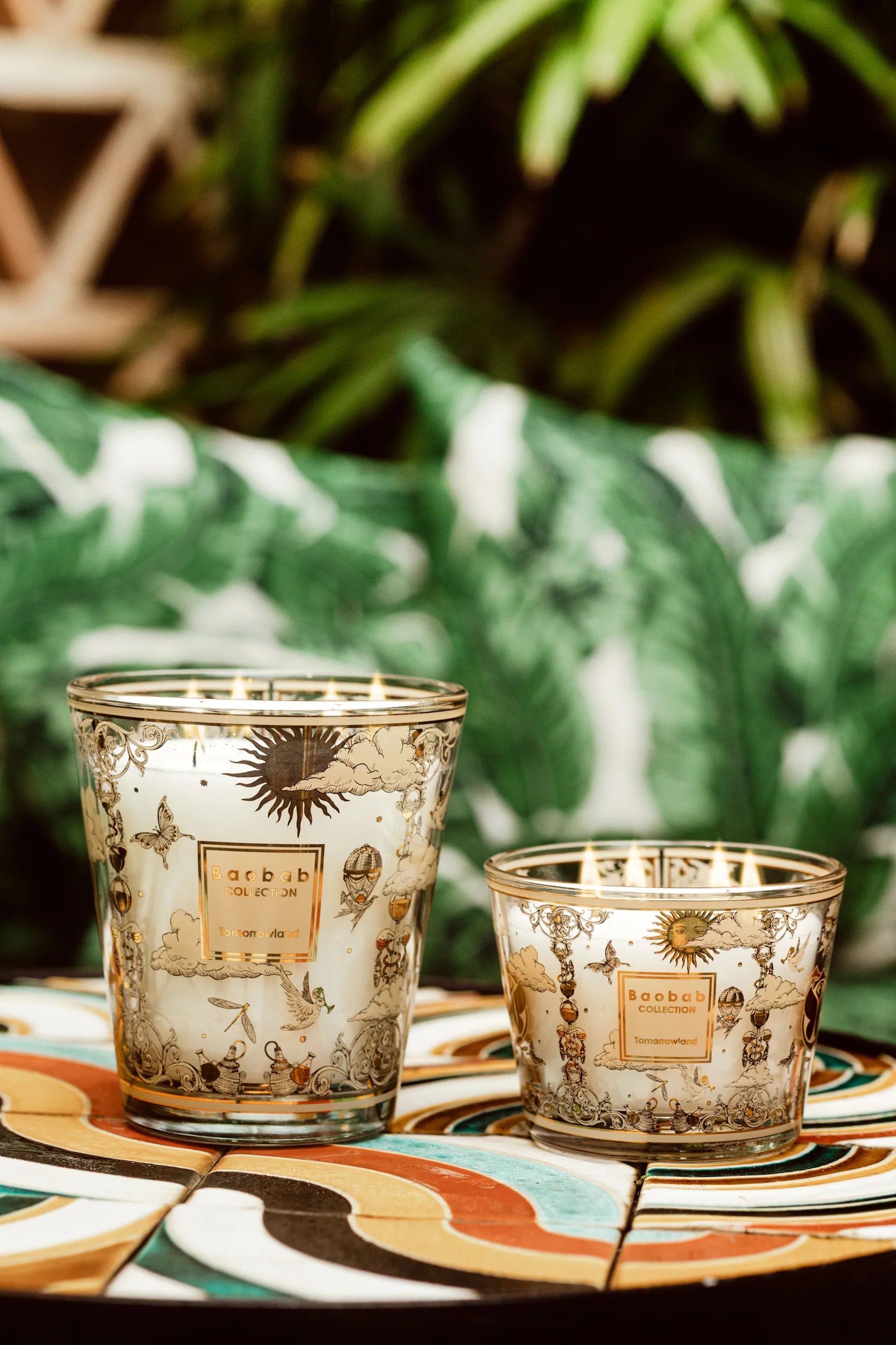 Baobab Collection scented candles with decorative glass designs on a vibrant table against a tropical backdrop.