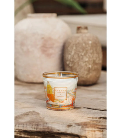 Baobab Collection scented candle with colorful print, placed beside rustic pottery on a wooden surface.